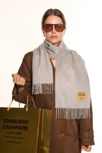 Close-up of hands presenting a neatly wrapped Edinburgh Cashmere scarf in a heritage-inspired gift box.